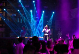 Glamorize Roma: Singer performs at a gay club in Rome, Italy. Blue spotlights illuminate the stage and crowd. Purple lighting adds to the ambiance.