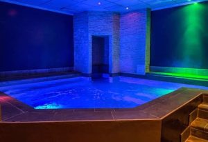 Metro Sauna Centrale Milan: Indoor pool with blue lighting, stone accents, and steps. Gay sauna for relaxation and socializing.