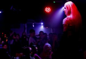 New Union Manchester: Drag queen performing at a gay club. Crowd watching under red and blue lights. Gay travel advice.