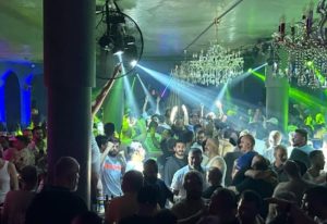 Stay Club Istanbul: A crowded gay club scene with men dancing under chandeliers and vibrant green & blue lights. Gay nightlife travel.