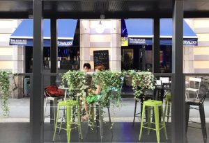 Sui Generis bar in Milan, Italy. Outdoor seating area, a popular gay-friendly spot. Blue awnings & lush greenery. Gay travel advice.