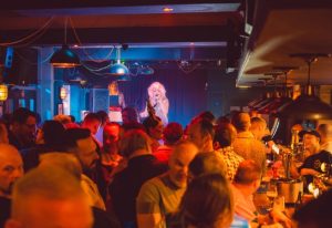 The Rem Bar, Manchester: Gay bar scene with a drag queen performing on stage. Crowd of men enjoying the show, drinks at the bar. Nightlife.