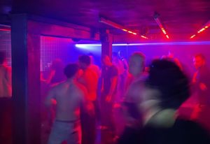 Trixie Copenhagen: Gay men dancing in a dark, crowded club with red and blue lighting. Nightlife scene, travel destination.