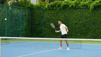 Santiburi Koh Samui tennis activity: Man playing tennis on a blue court at the Maenam resort. Gay travel advice for active vacations.