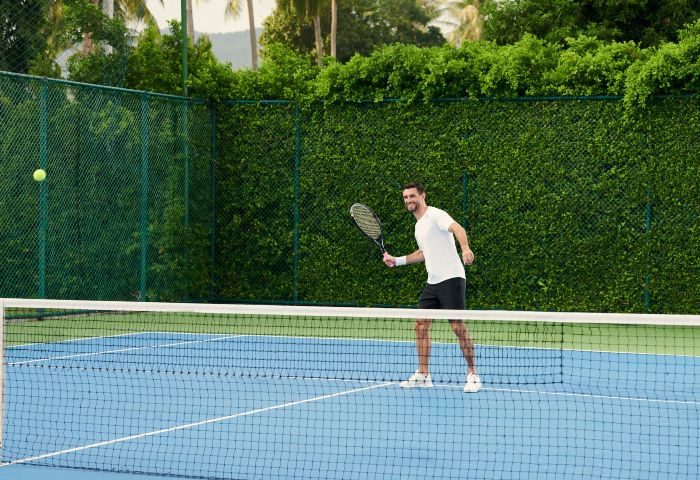 Santiburi Koh Samui tennis activity: Man playing tennis on a blue court at the Maenam resort. Gay travel advice for active vacations.