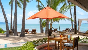 Deluxe Beachfront Villa patio at Santiburi Koh Samui. Plunge pool view, palm trees, beach chairs, orange umbrella, table with drinks, hammock.
