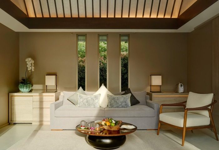 Santiburi Koh Samui Grand Reserve living room. Luxury gay travel in Thailand. Elegant suite interior, sofa, table, and view of lush greenery.