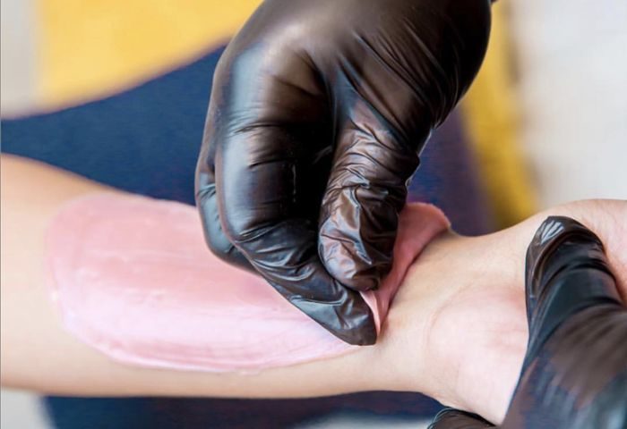 AlexSpot24: Man's arm being waxed. Pink wax is applied by hands in black gloves. Gay travel advice: grooming tips for smooth skin.