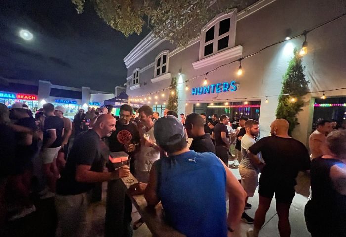 Hunters Wilton Manors: Outdoor patio scene at the gay bar. Crowd of men socializing under string lights at night. Gay travel destination.