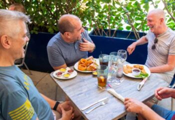 Gay men enjoy food at Rosie's Bar & Grill. The 1-6.jpg image shows a group laughing over onion rings, sandwiches, and chicken tenders.
