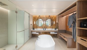 SAii Laguna Phuket Lagoon View Suite bathroom. Modern design with tub, shower, double sinks, and closet. Ideal for gay travel, offering luxury and style.