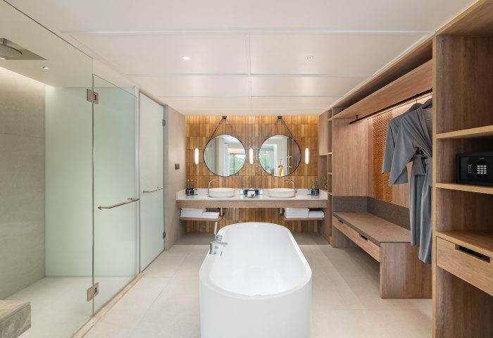 SAii Laguna Phuket Lagoon View Suite bathroom. Modern design with tub, shower, double sinks, and closet. Ideal for gay travel, offering luxury and style.