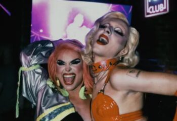Drag queens at 101 Club Roma, a gay bar. Two performers with heavy makeup and costumes pose, smiling and expressive, in the club's atmosphere.