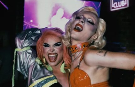 Drag queens at 101 Club Roma, a gay bar. Two performers with heavy makeup and costumes pose, smiling and expressive, in the club's atmosphere.