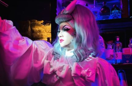 Drag queen at 101 Club Roma, a gay bar in Rome, Italy. Pink lighting highlights the performer's makeup and costume. Gay travel advice.