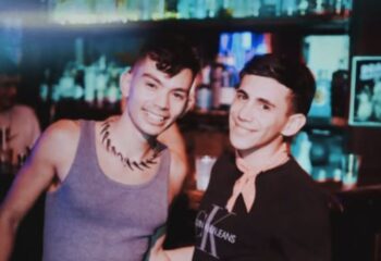 Two gay men smiling at 101 Club Roma. Nightlife scene with bar background. Gay travel advice, gay bar, Roma nightlife.