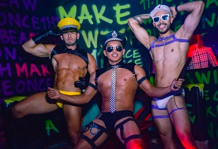 Cancun gay bar 11-11 Club photo. Three shirtless men in underwear and police hats pose at the gay nightclub. Nightlife for gay men in Cancun.