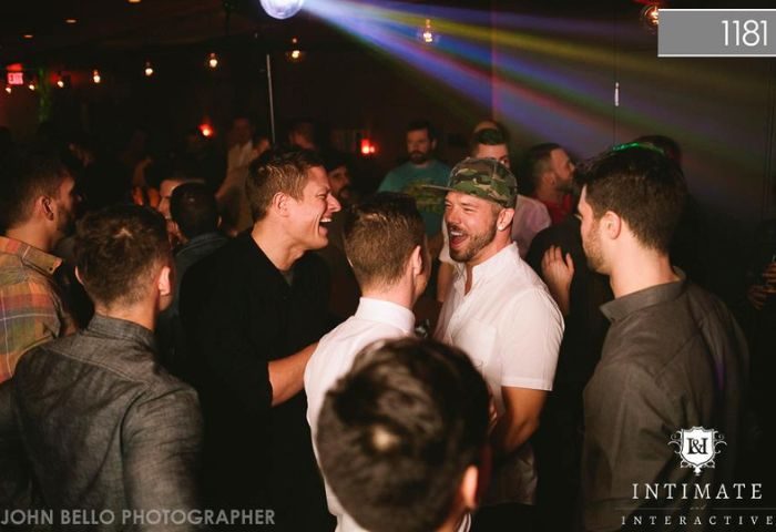 Gay Vancouver nightlife: Men laughing at 1181 Lounge, a popular gay bar. Rainbow lights and a disco ball create a fun atmosphere.