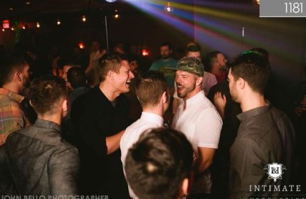 Gay Vancouver nightlife: Men laughing at 1181 Lounge, a popular gay bar. Rainbow lights and a disco ball create a fun atmosphere.