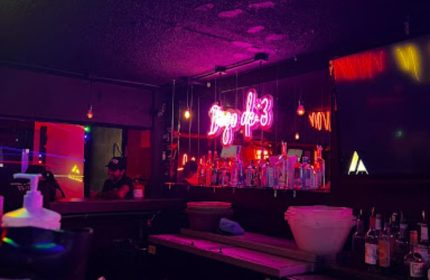 Inside 11:11 Club, a gay bar in Cancun. Neon signs, bottles on the bar, and a bartender create a vibrant, inviting atmosphere.