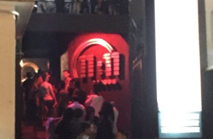 Entrance to 11:11 Club, a gay bar in Cancun, Mexico. People are gathered near the entrance. Red lighting highlights the club's logo.