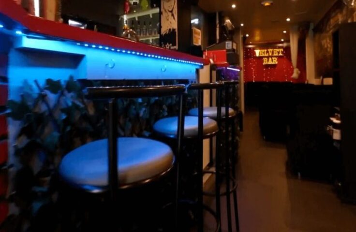 Interior of Le Velvet bar, a gay travel destination. Bar stools line the counter with blue LED lights. Velvet Bar sign visible in the background.