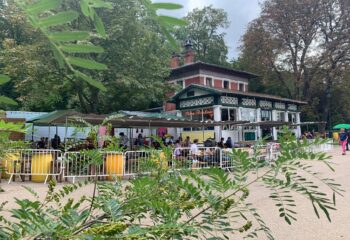 Rosa Bonheur: Outdoor Parisian cafe scene. People at tables, greenery, and architecture. Popular gay-friendly spot for drinks and socializing.