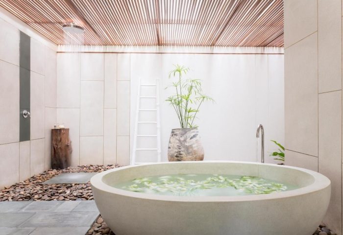 The Sarojin Khao Lak: Outdoor bathroom with a round tub filled with flowers, shower, pebbles, and plant. Gay travel luxury at its finest.