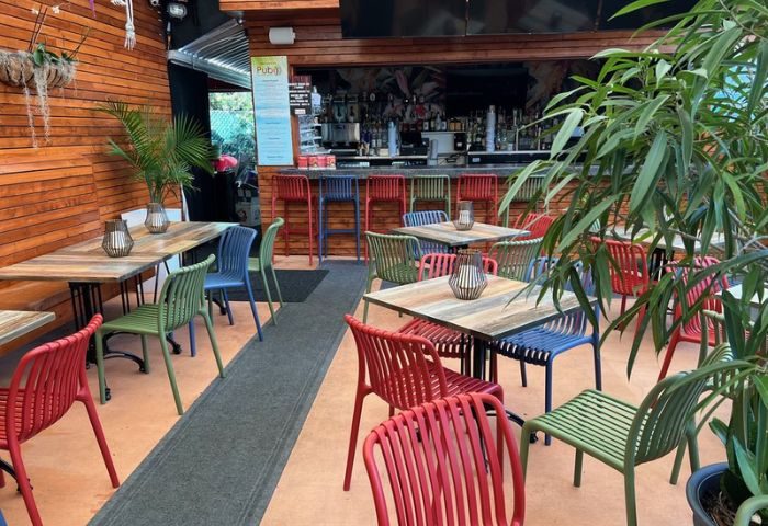 Outdoor dining area at The PUB Wilton Manors. Colorful chairs and wooden tables create a vibrant, welcoming space for gay travelers. Bar in background.