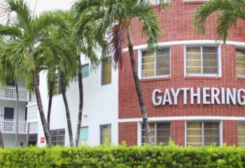 Hotel Gaythering's exterior. A gay bar and hotel with palm trees. Brick building with GAYTHERING sign. Gay men travel destination.