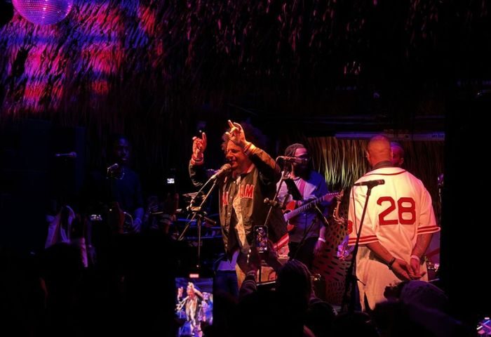 Gramps at a gay bar. A singer performs on stage with a band, under a disco ball. Audience members record the performance on their phones.
