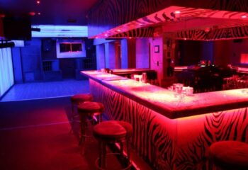 Interior of Twist gay bar with zebra print, red and blue lights. Stools line the bar. Gay travel advice.