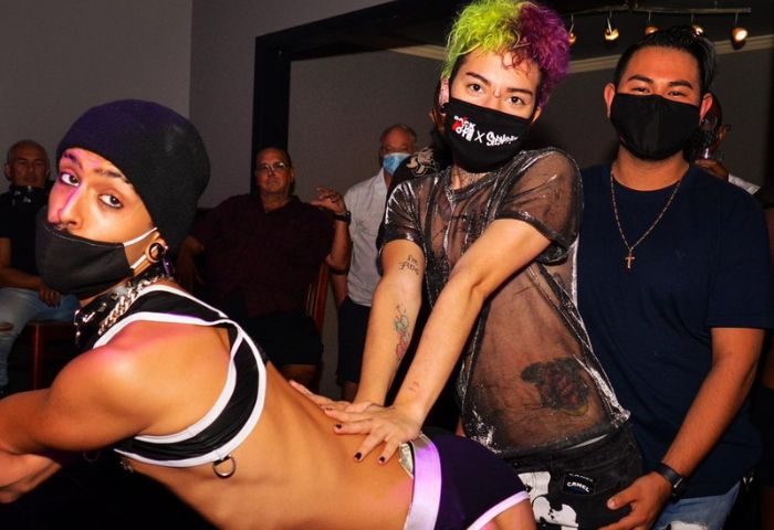 LeBoy 2-4: Gay men in masks at a party, one in a harness and beanie, another with colorful hair and tattoos, and a third with a cross necklace.