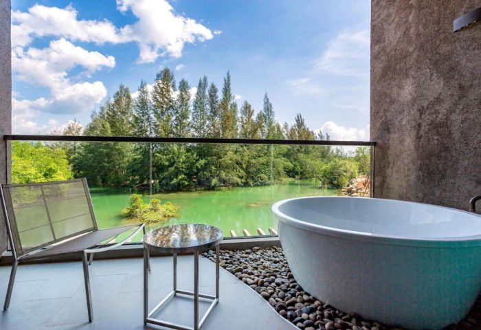 Kalima Resort Khao Lak balcony view. Bathtub, chair, and table on patio overlooking lush greenery. Gay travel relaxation and luxury.