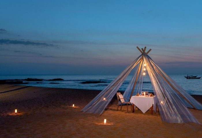 Romantic beach dinner at La Vela Khao Lak. A tent with lights and a table set for two on the sand at dusk, perfect for gay couples.