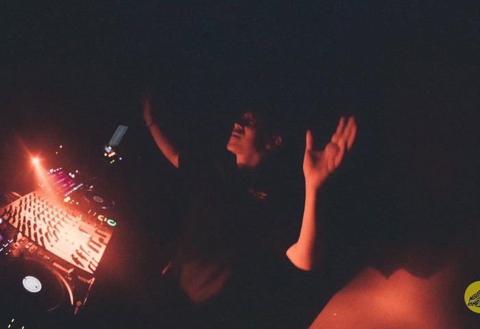 Gay travel: DJ with arms raised at a dark party. Nightlife scene with music and dance. Potent event for gay men.