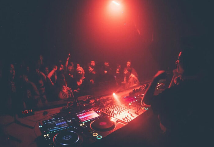 Gay nightlife: DJ performing at a potent party. Red lighting, crowd dancing. Gay travel advice.