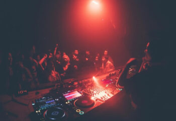 Gay nightlife: DJ performing at a potent party. Red lighting, crowd dancing. Gay travel advice.