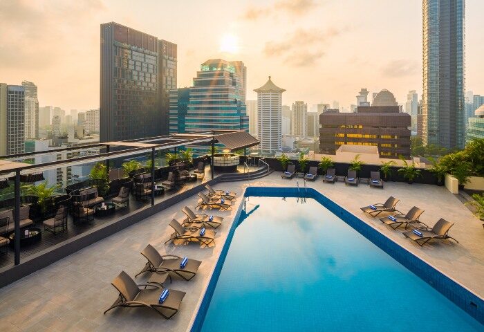Rooftop pool at voco Orchard Singapore, an IHG Hotel, in the evening. Lounge chairs line the pool's edge, with city views. Gay travel.