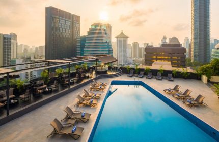 Rooftop pool at voco Orchard Singapore, an IHG Hotel, in the evening. Lounge chairs line the pool's edge, with city views. Gay travel.