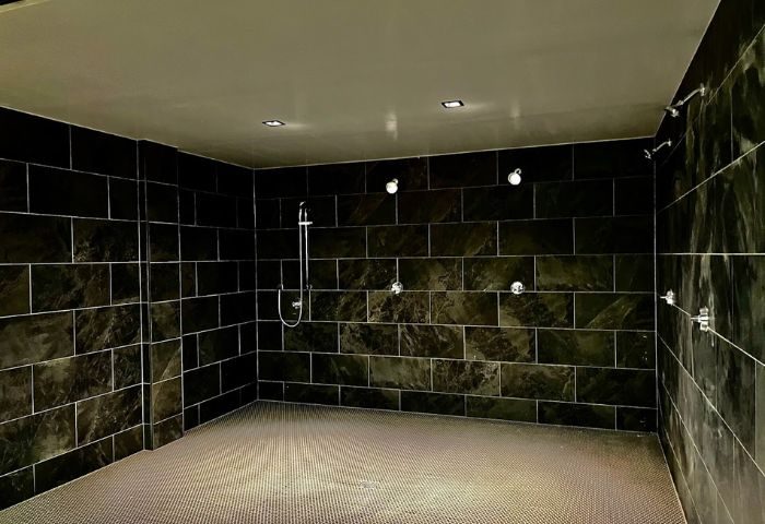 Wilton Social Club's communal shower room. Dark tiled walls, multiple shower heads, and a textured floor. Gay travel advice.