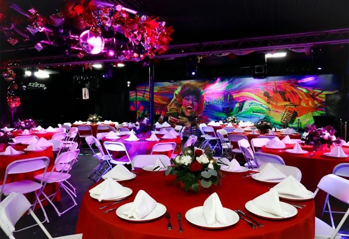 Azucar Nightclub's interior. Red tablecloths, white chairs, floral centerpieces, and a vibrant stage backdrop. Gay nightlife event space.