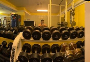 Club Aqua gym: Dumbbell rack with weights ranging from 75 to 105. Man taking a selfie in the mirror. Gay travel fitness.