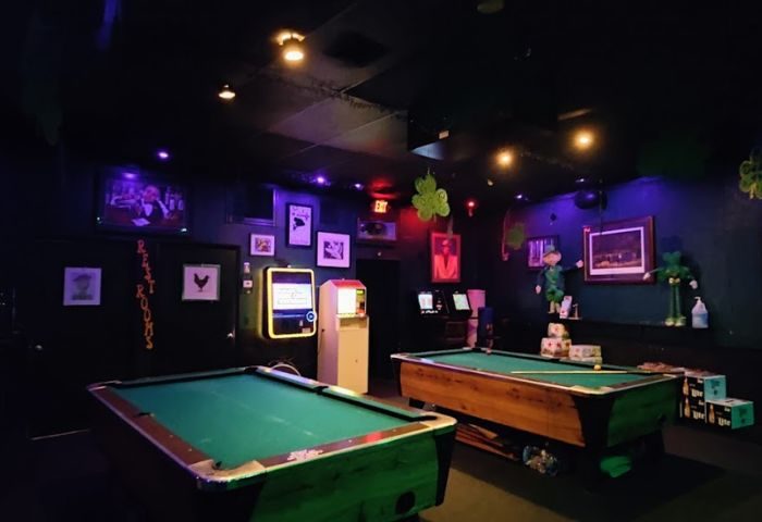 The Corner Pub: Interior shot of a gay bar with two pool tables. Shamrock decorations, arcade games, and dark lighting. 3-2.jpg.