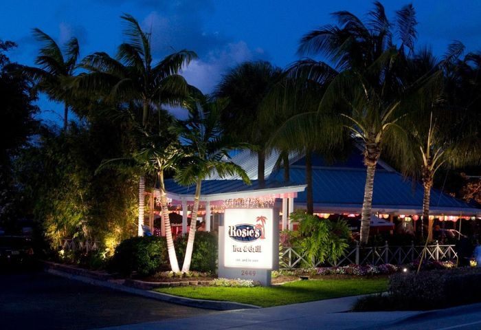 Rosie's Bar & Grill at night. Palm trees surround the illuminated sign. A popular gay bar and restaurant for gay men's travel in Florida.