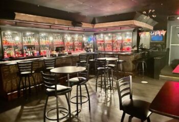 Interior of The Eagle Wilton Manors bar. Bottles on shelves behind the bar, tables and chairs in the foreground. Gay bar in Wilton Manors.
