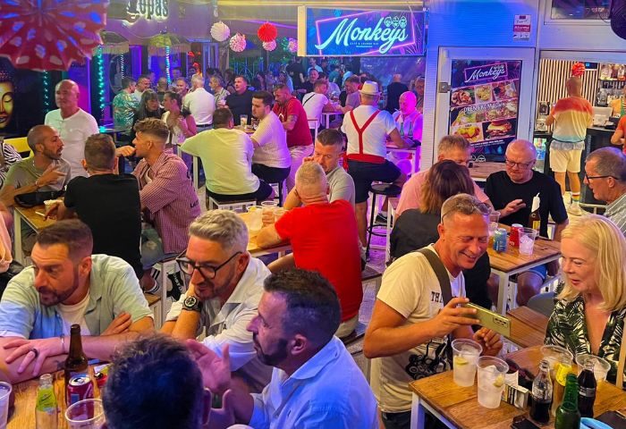 Gay bar scene at 3 Monkeys in Torremolinos. Crowded outdoor seating area with men enjoying drinks. Popular gay nightlife destination.