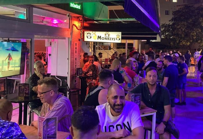 Gay bar 3 Monkeys in Torremolinos, Spain. Crowd of gay men socializing at tables outside. Popular gay travel destination.