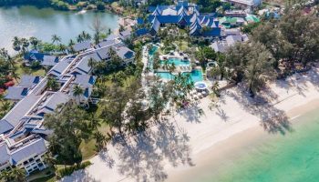 Aerial view of SAii Laguna Phuket resort. Beachfront property with pools, palm trees, and traditional Thai architecture. Ideal for gay travel.