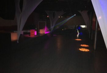 Interior of Club Boi, a gay bar. Features white draping, colorful stage lights, and a dark dance floor. Gay travel destination.